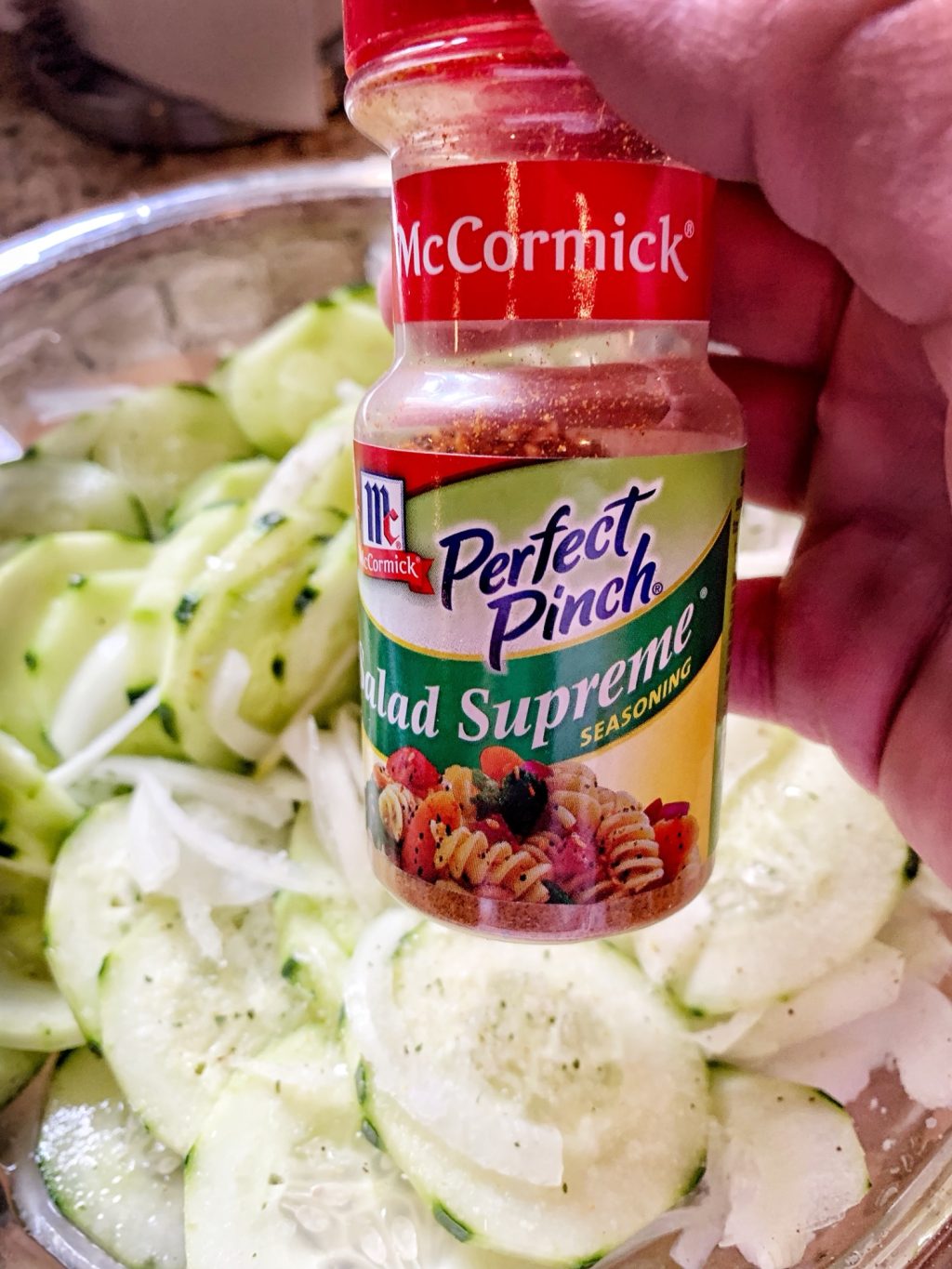 A small bottle of Perfect Pinch Salad Supreme Seasoning held over the cucumber salad