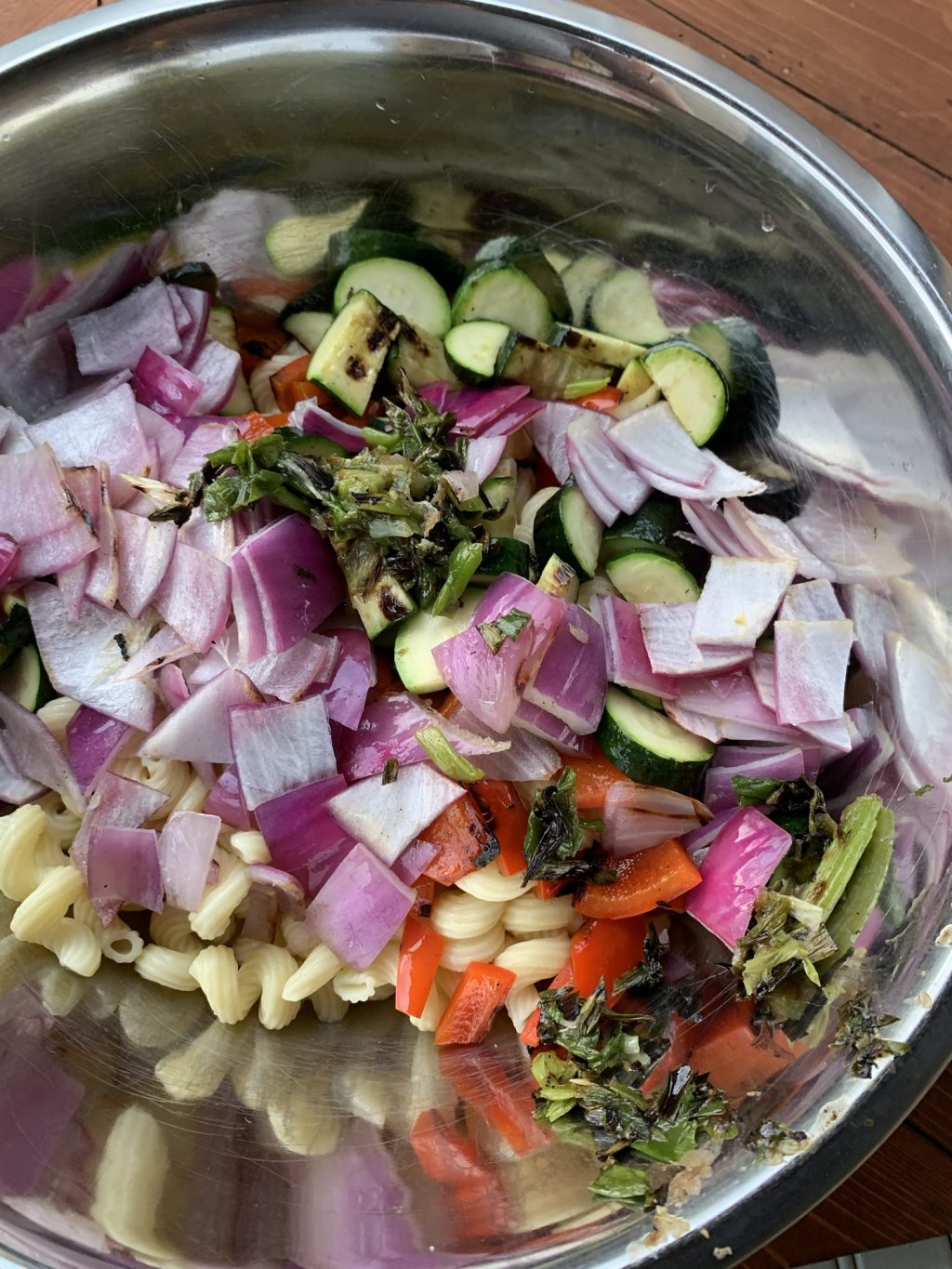 The chopped grilled vegetables on top of the cooked pasta in a metal bowl