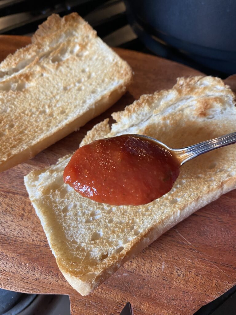 A spoon of tomato sauce held over two toasted slices of bread