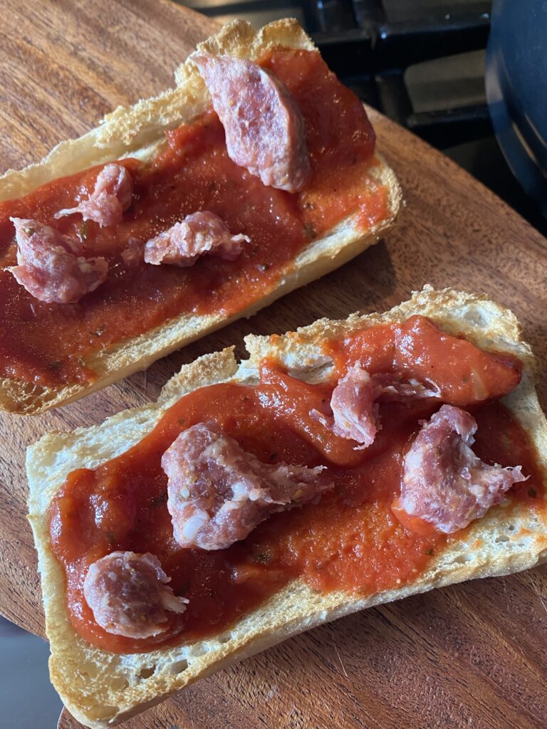 Clumps of sausage on top of pizza sauce spread over toasted bread