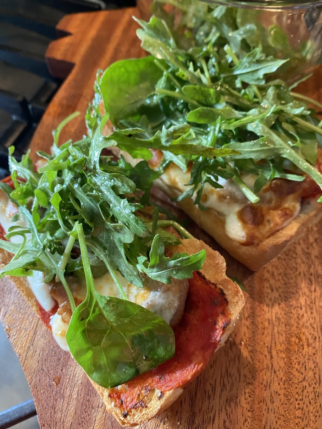 Two pieces of toasted bread with tomato sauce, cheese, and greens