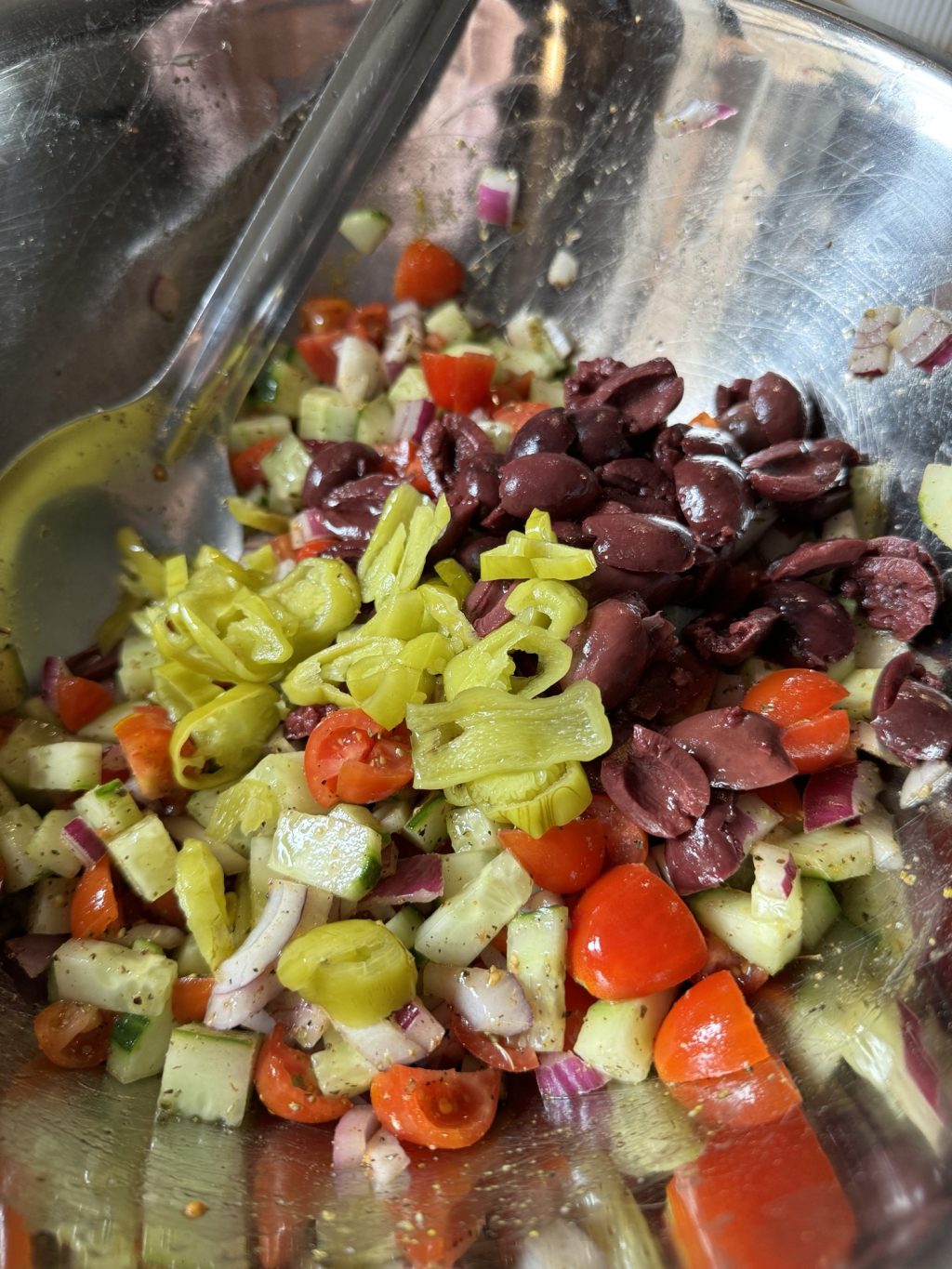 Chopped and marinated tomatoes, olives, cucumbers, peppers, and onions in a metal bowl