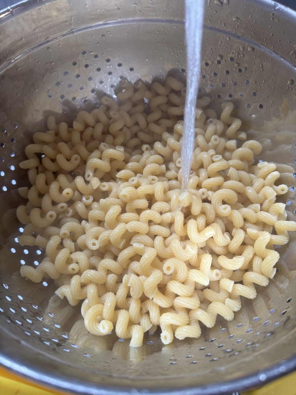 Pasta in a strainer being washed with tap water