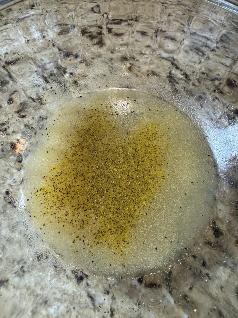 A lemon juice dressing with seasonings in a glass bowl