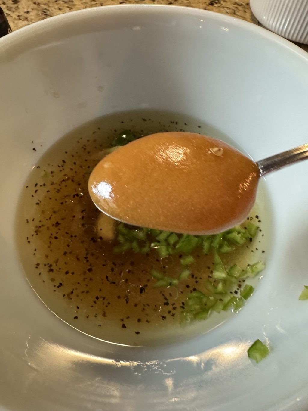 A spoon of honey held over a mixture of vinaigrette and diced jalapeno