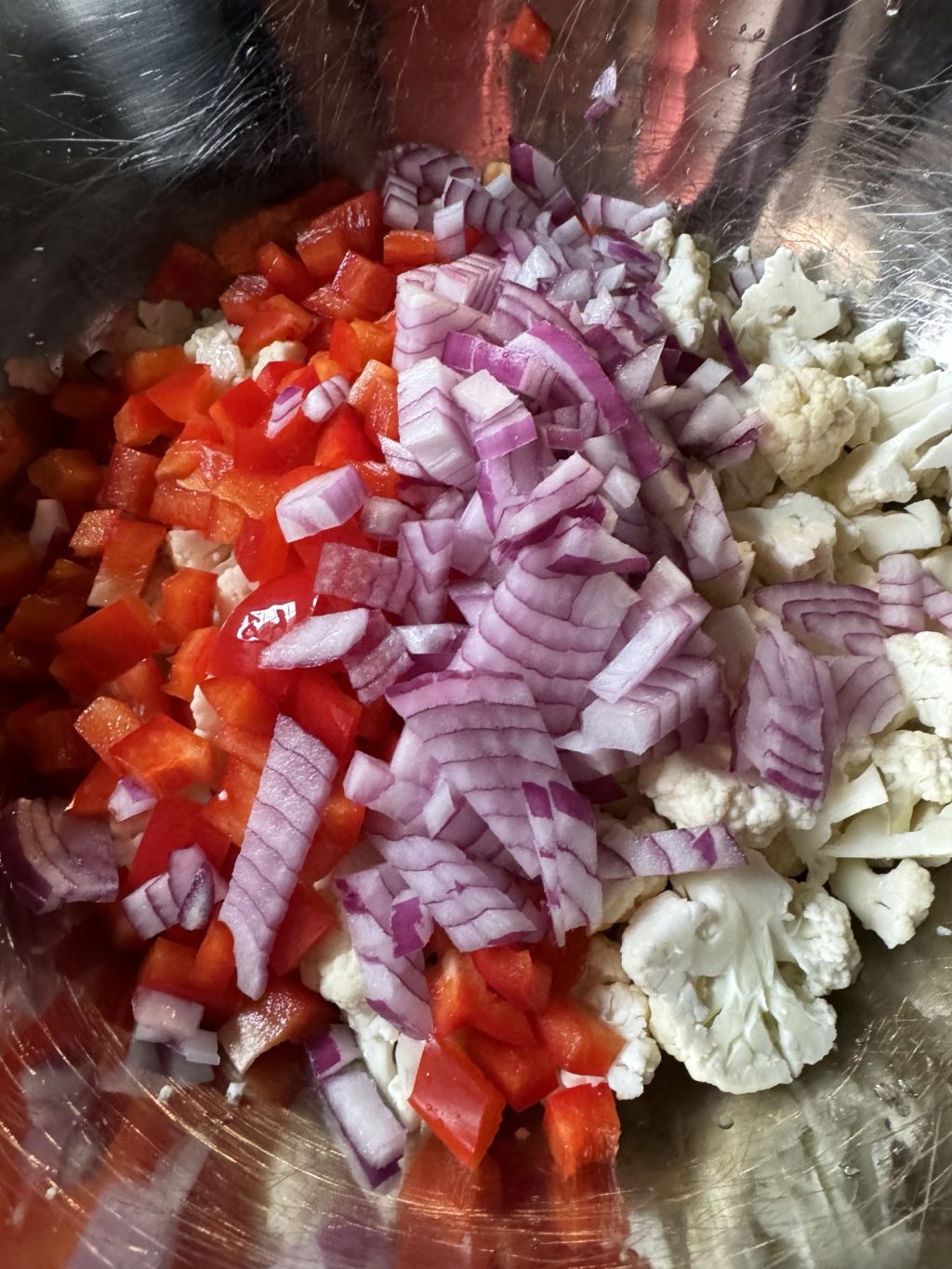 A mix of chopped red bell pepper, onions, and cauliflower in a metal bowl