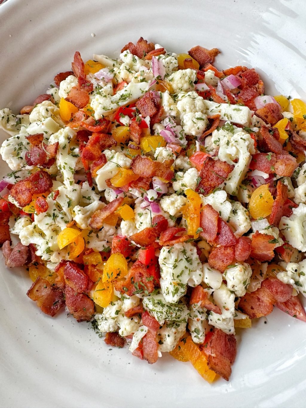 Cauliflower, chopped bacon, and crunchy vegetables in a white bowl