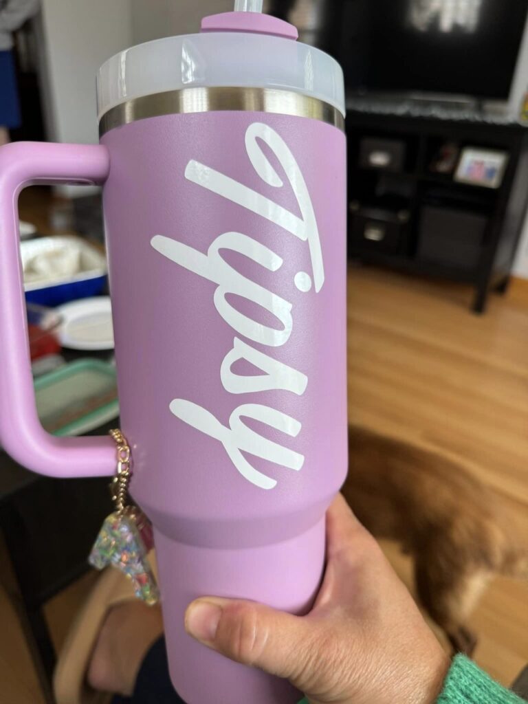 A pink travel mug with "Tipsy" written in white on the side.