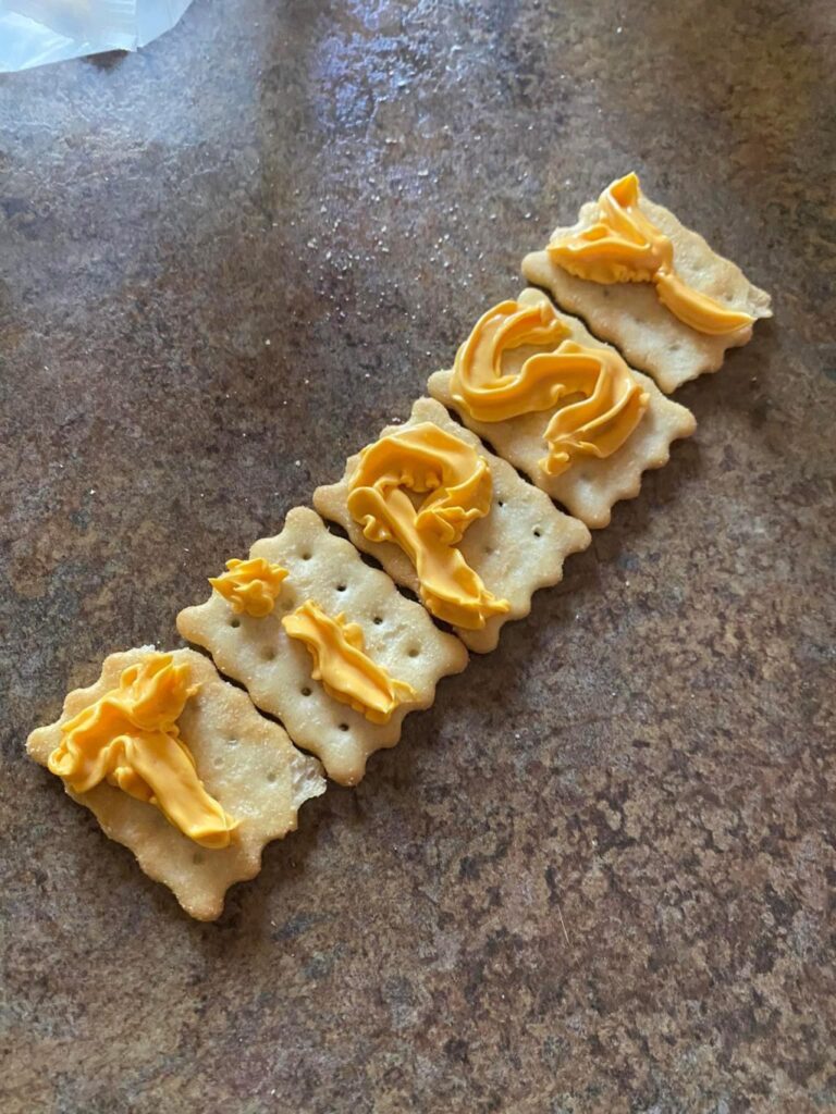 Five crackers with the letters for "Tipsy" sprayed on each one in spray cheese.