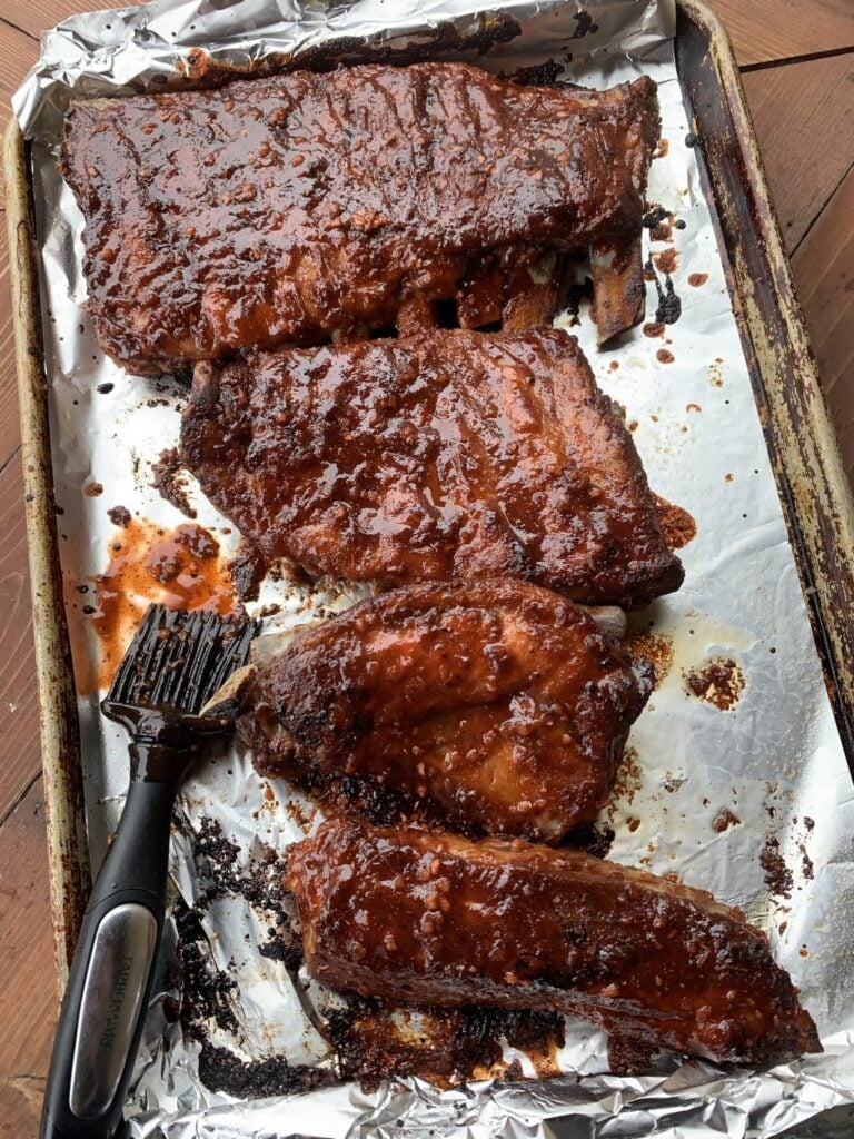 Ribs on a baking sheet with a sauce brush.