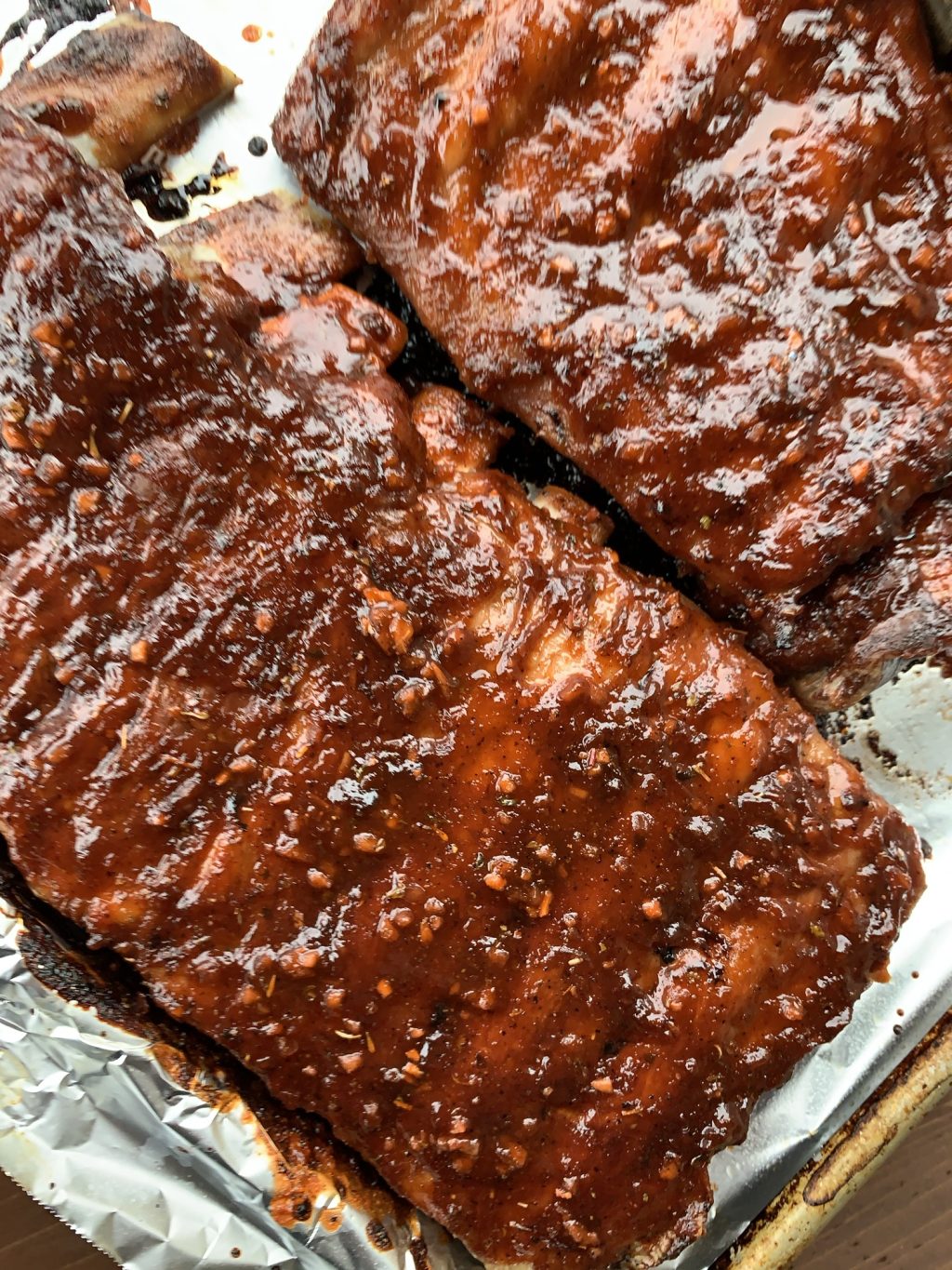 Two racks of ribs on a baking sheet with BBQ sauce spread over them.