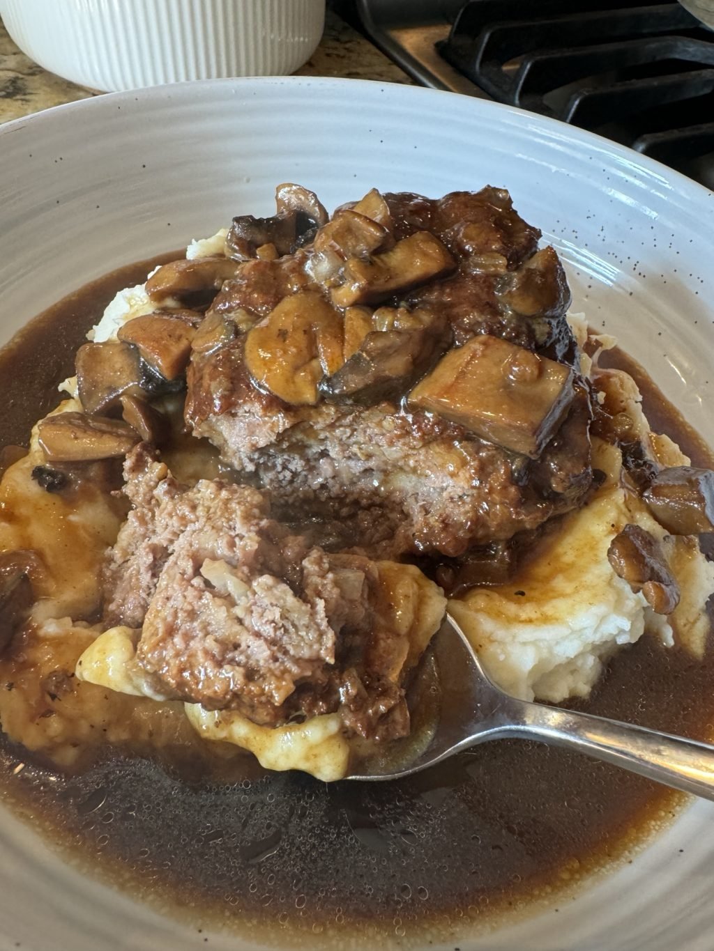 Salisbury Steak over mashed potatoes with gravy and mushrooms with a spoon taken out of it