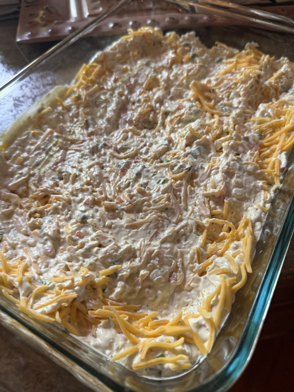 A glass baking dish with the various dip ingredients, including shredded cheese, cream cheese, and diced veggies