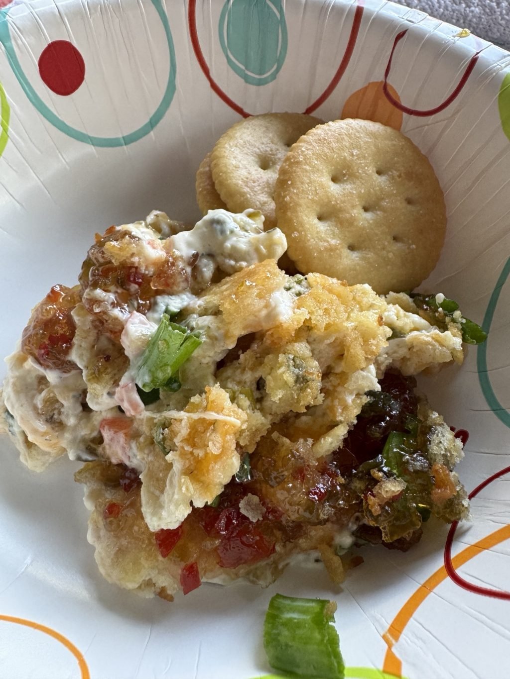 A paper bowl of the World's Best Party Dip with three Ritz crackers