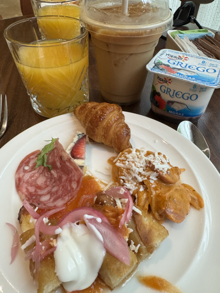 A plate from the breakfast buffet with various foods, including a mini croissant, and apple pastry, and a piece of salami.