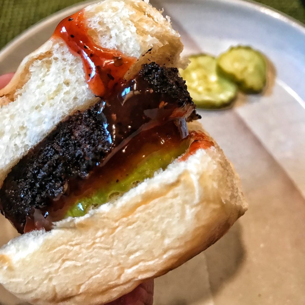 A close up of a pork tenderloin slider with pickles and BBQ sauce.