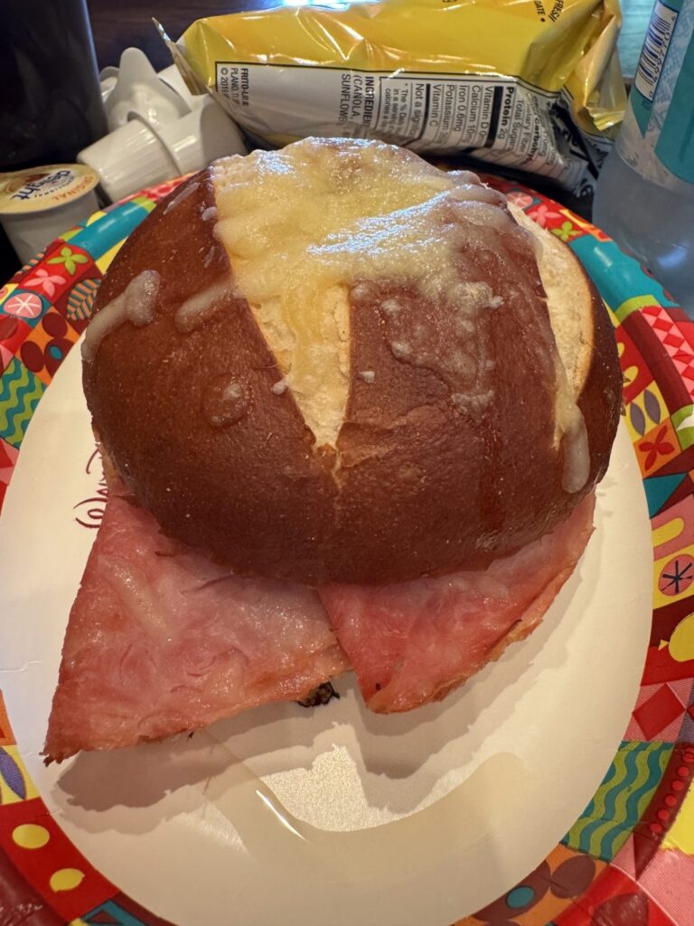 A ham and cheese sandwich with a bag of potato chips behind it.