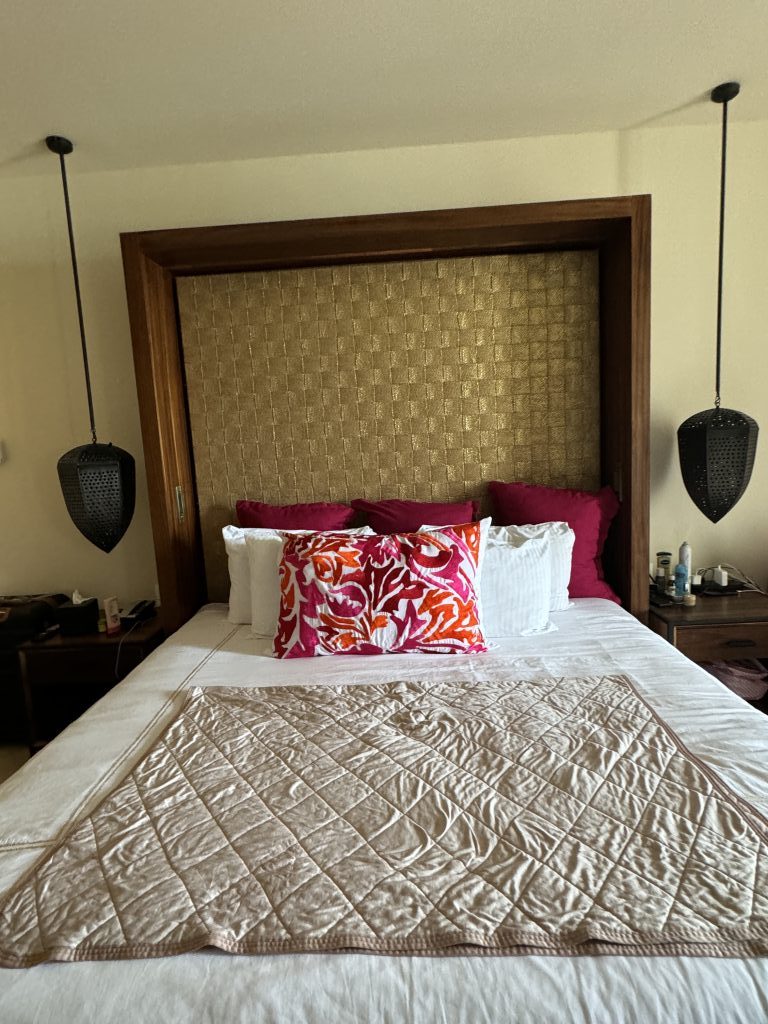 A hotel bed with multiple red and white pillows and a black hanging lamp on either side.
