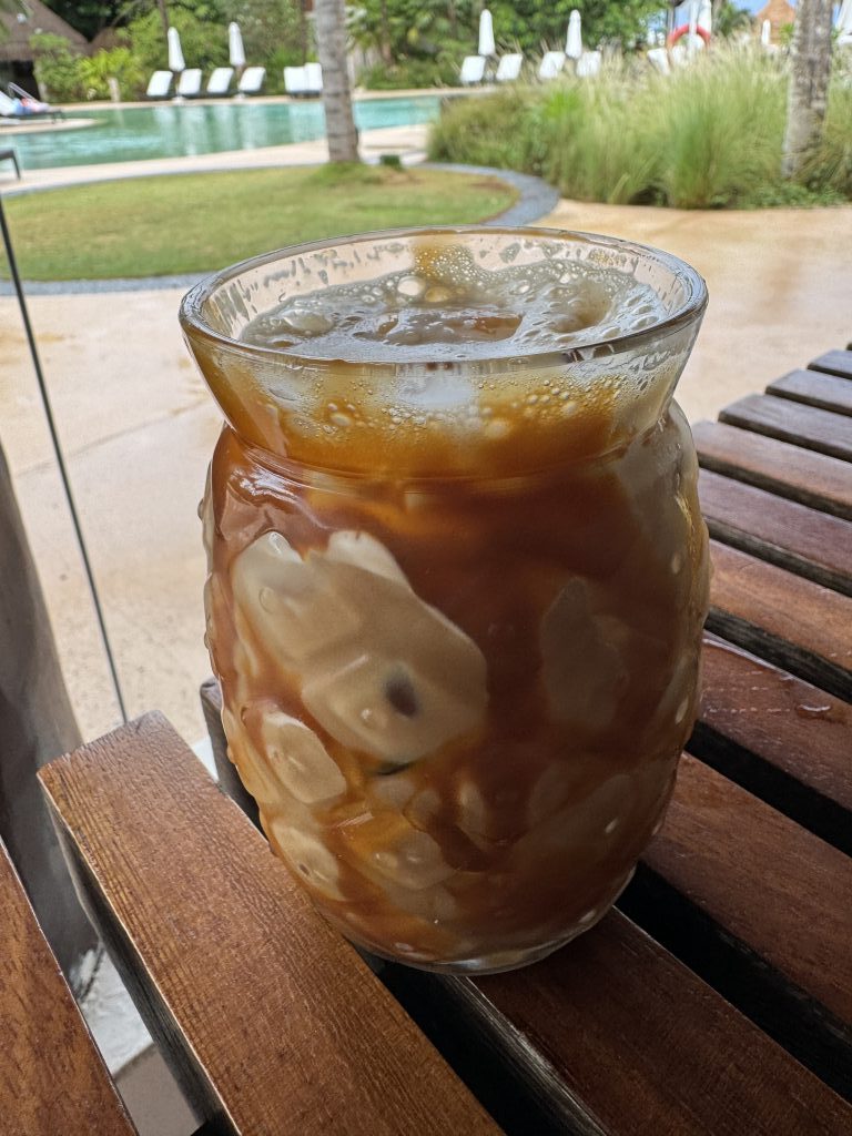Iced coffee in a pineapple shaped glass on a table by the pool.