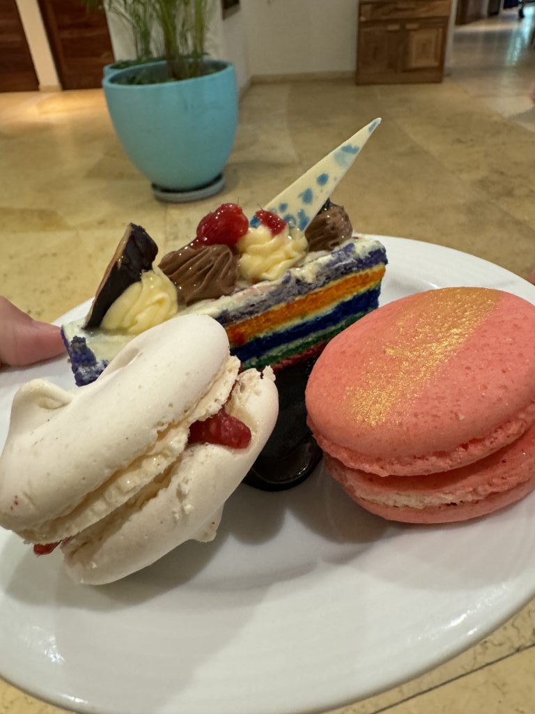 A selection of colorful desserts, including two macarons and an orange and blue slice of layer cake.