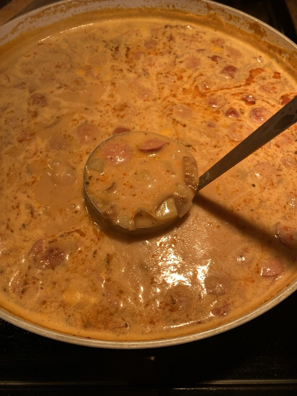 A ladle over frankfurter and potato soup over a pot full of it.