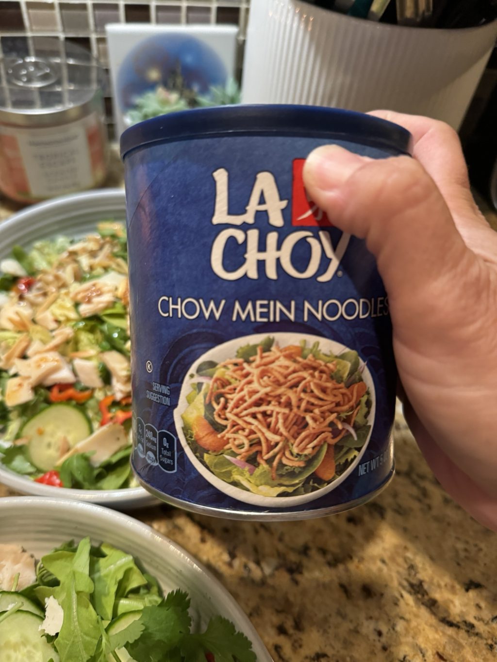 A container of La Choy Chow Mein Noodles being held above the salad.