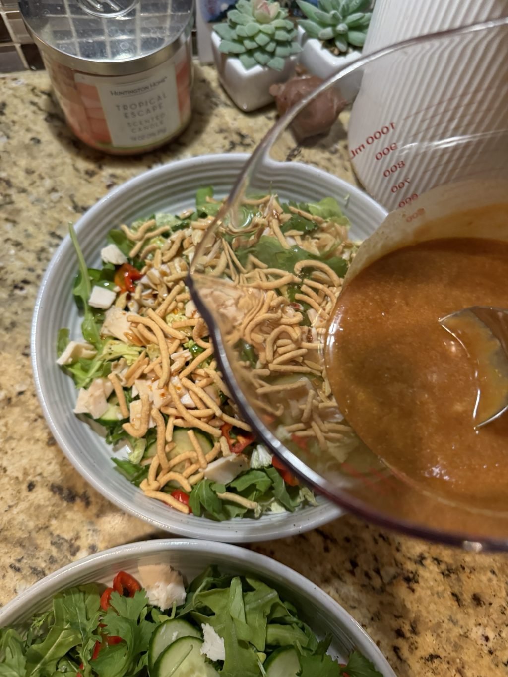 The peanut dressing being held above the Chinese chicken salad about to be spooned on to it.