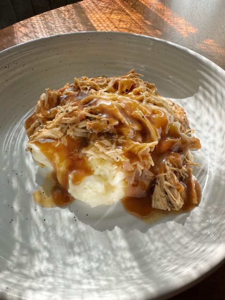 Shredded chicken in gravy on top of mashed potatoes.