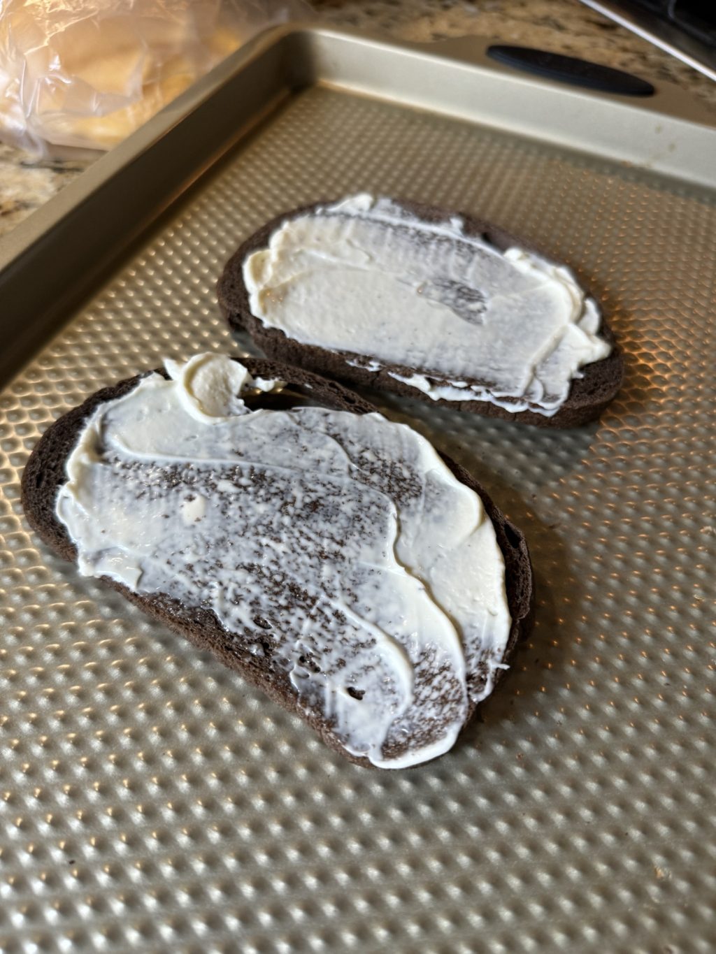 Two slices of pumpernickel bread with mayo spread on each.