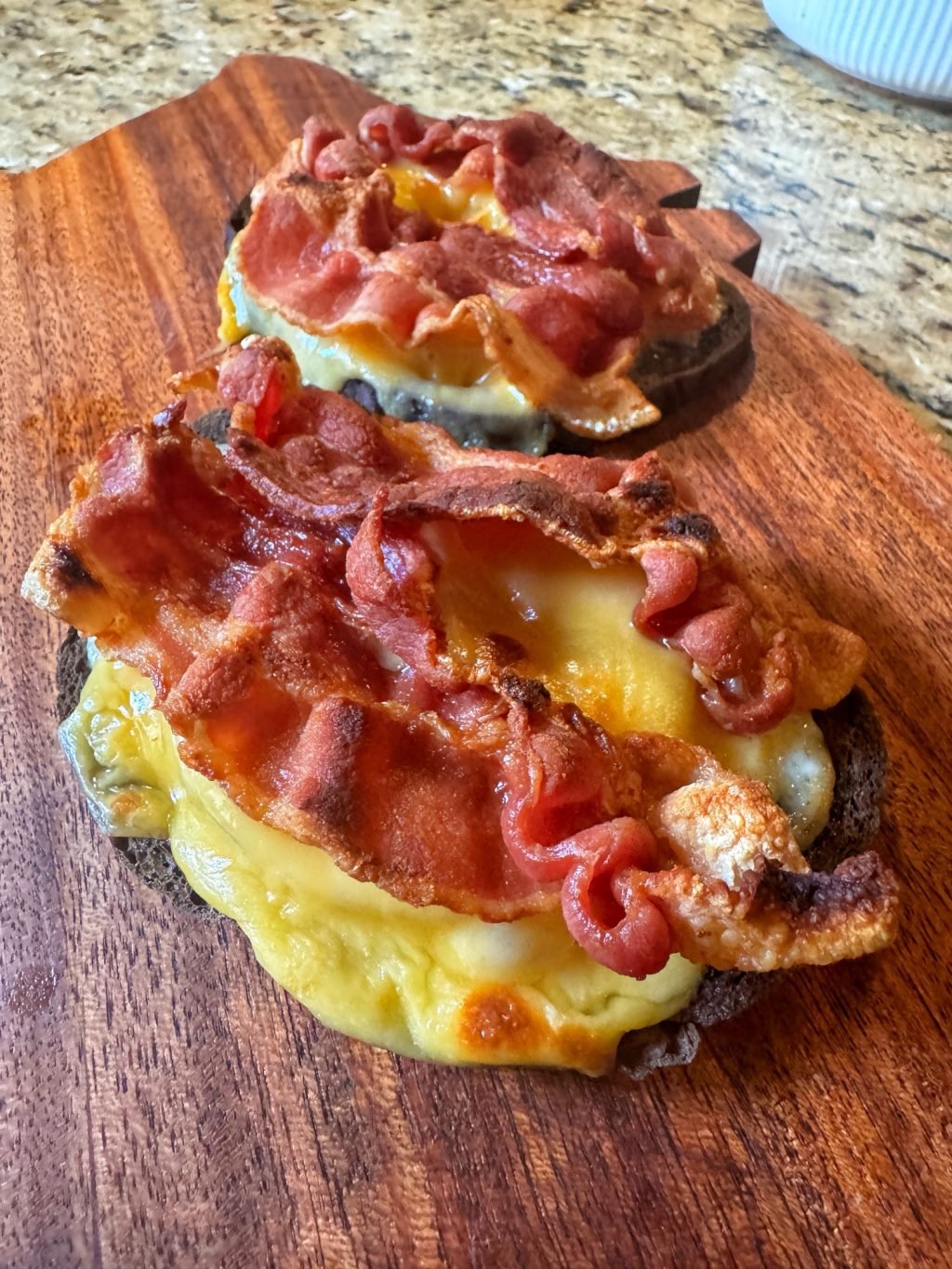 Two open faced sandwiches with bacon over melted cheese and pineapple.