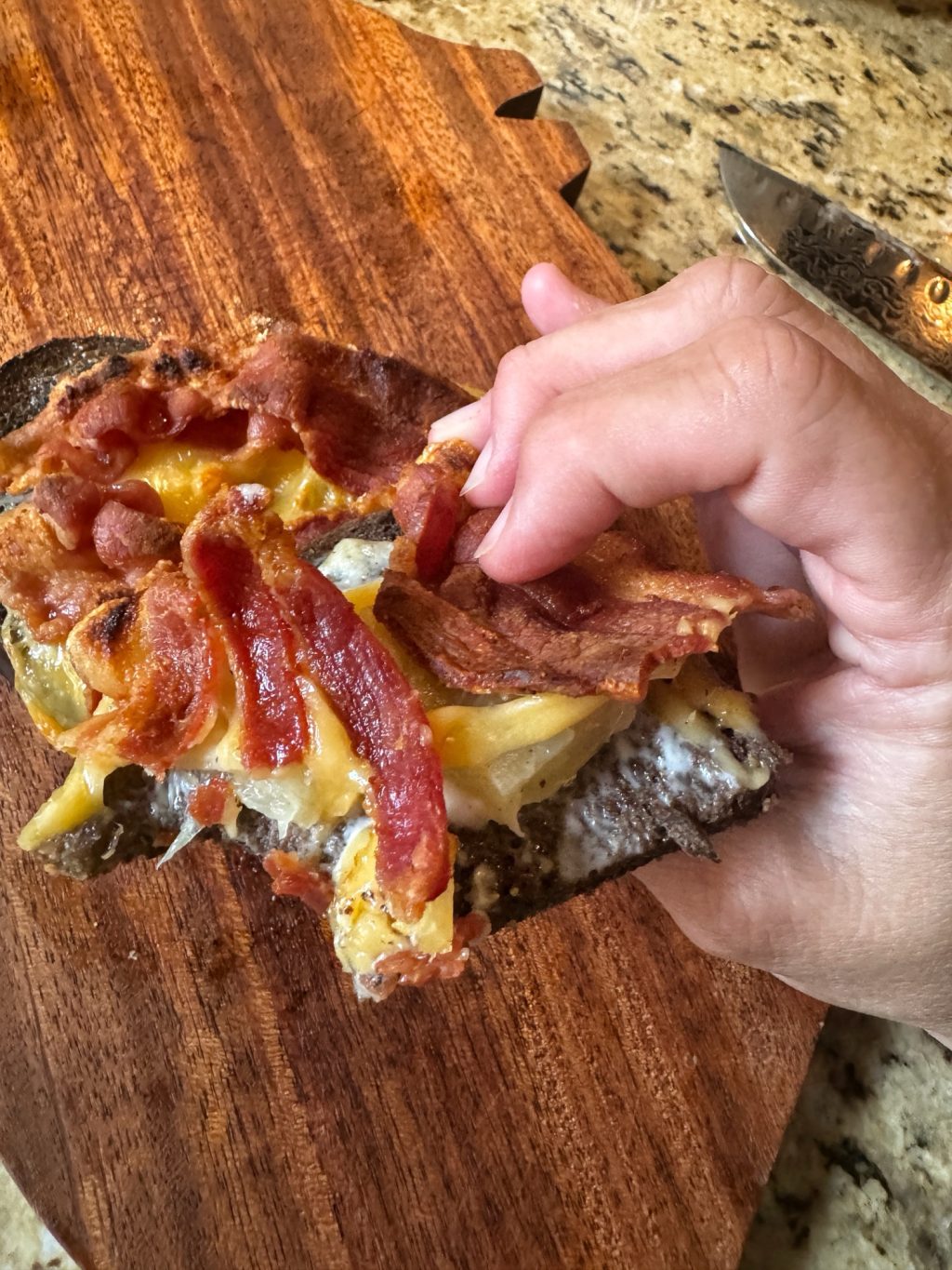 An open faced sandwich with pineapple, bacon, and cheese with a bite taken out of it.