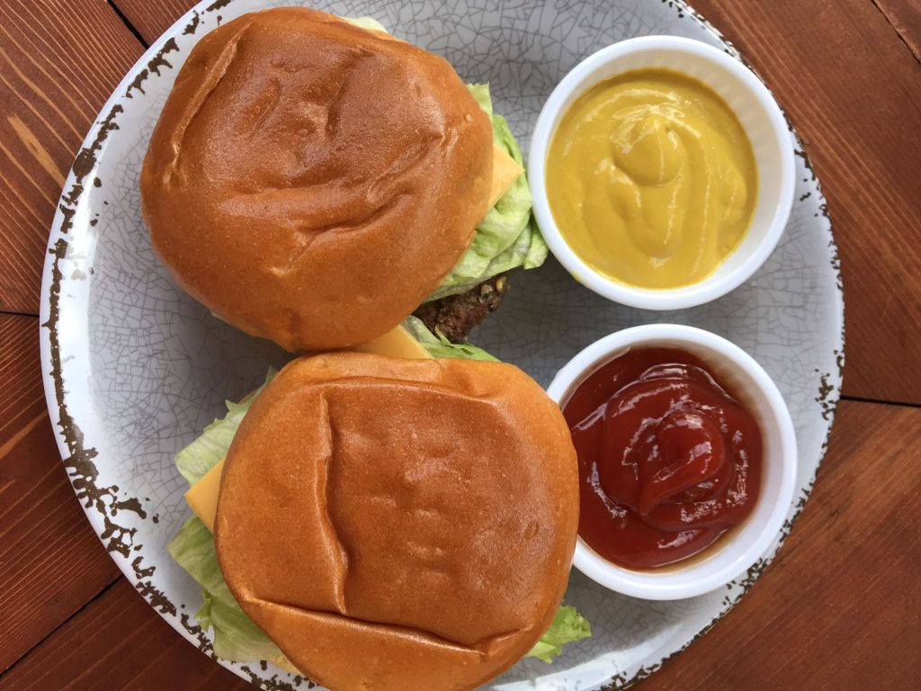 An overhead shot of two cheeseburgers on a plate with cups of mustard and ketchup.