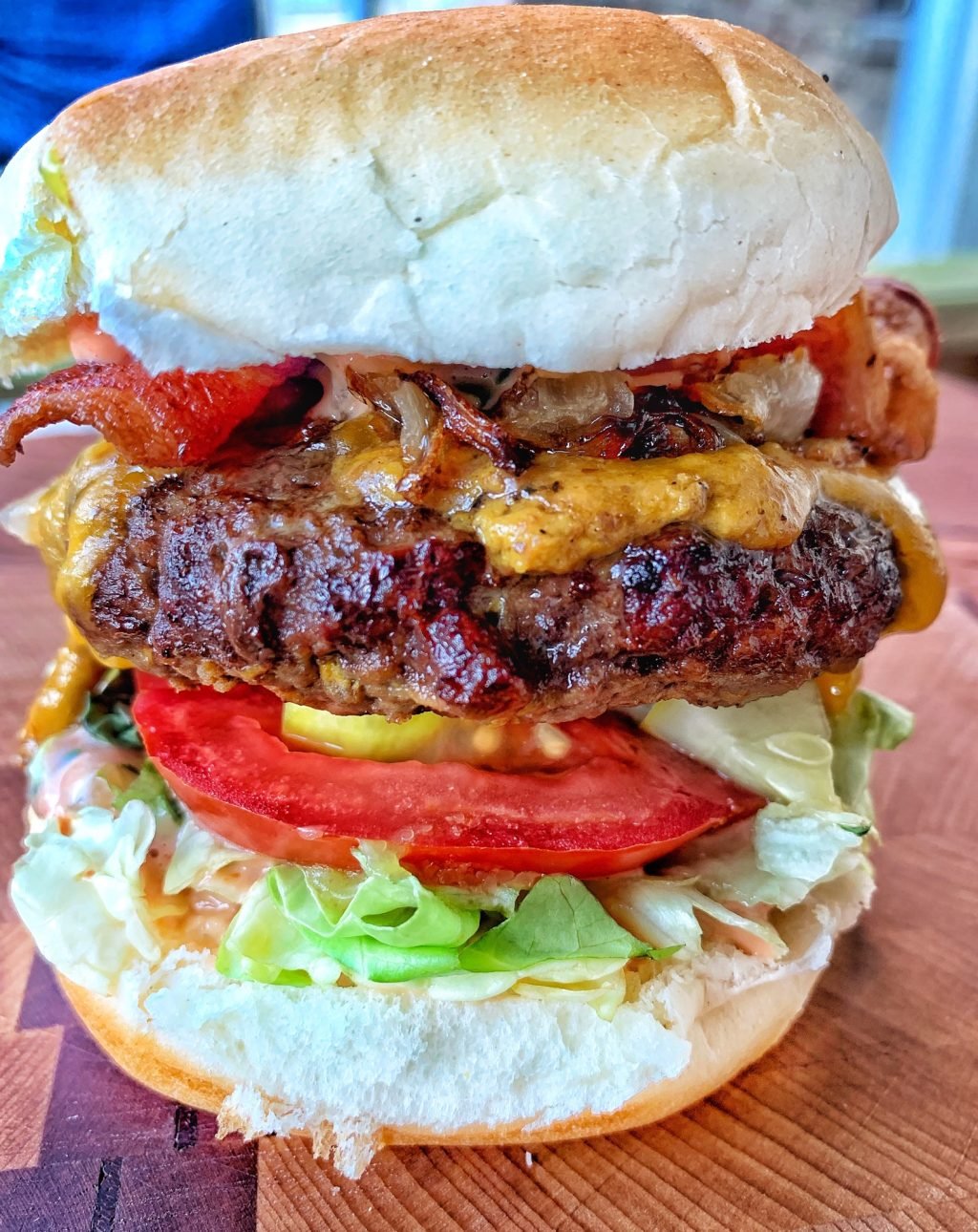 A close up view of a cheeseburger with lettuce, tomato, cheese, cooked onions, and bacon.