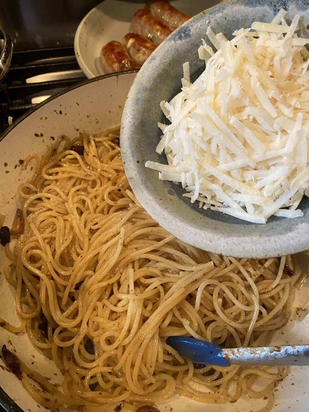 A container of shredded cheese being poured into a bowl of spaghetti.