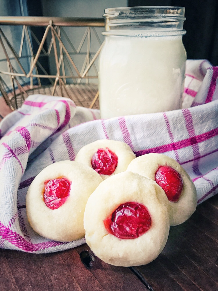 Butter cookies with cherries and a glass of milk.