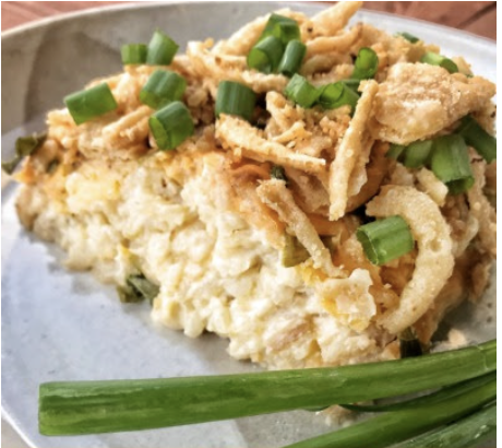A close up of a slice of crockpot potato casserole on a plate with green onions and crispy onions on top.