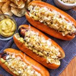 Three hot dogs with mustard, kraut, and crushed chips on top.