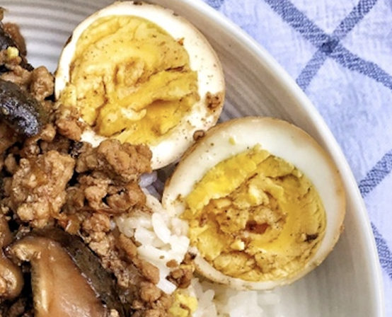 A hard boiled egg split in haf on the side of the plate of ground pork and rice.