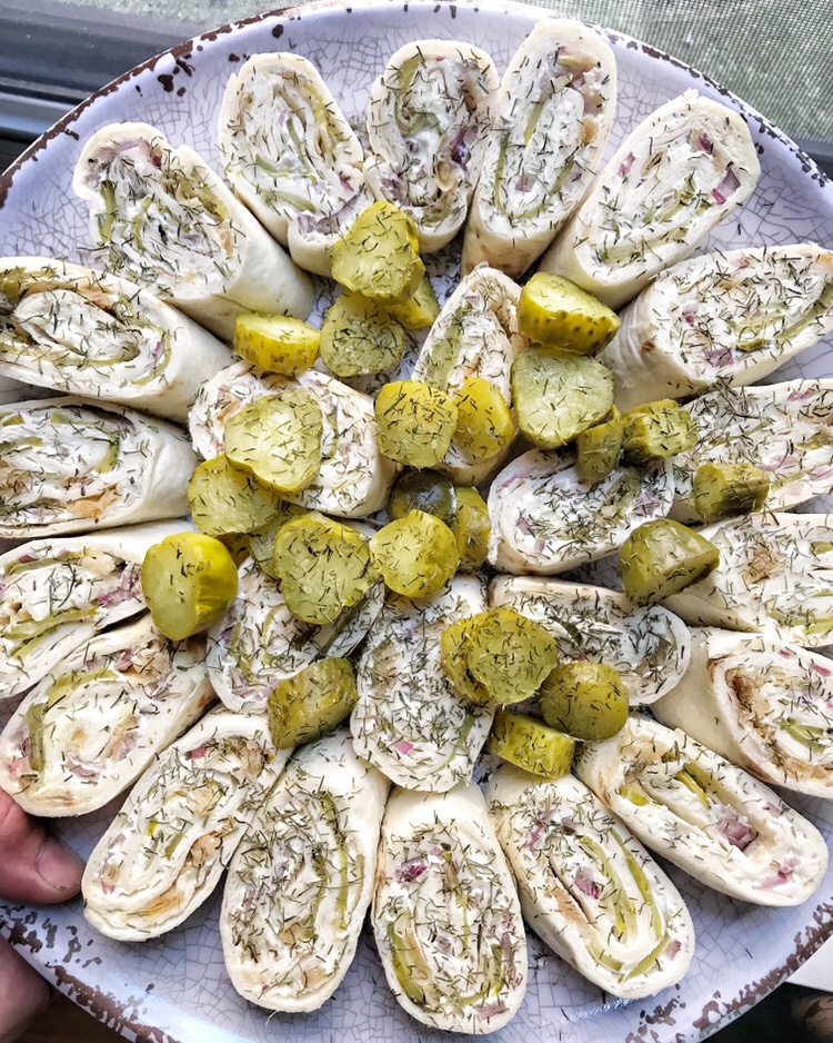 Pickle pinwheels spread out on a plate with pickle slices in the middle.