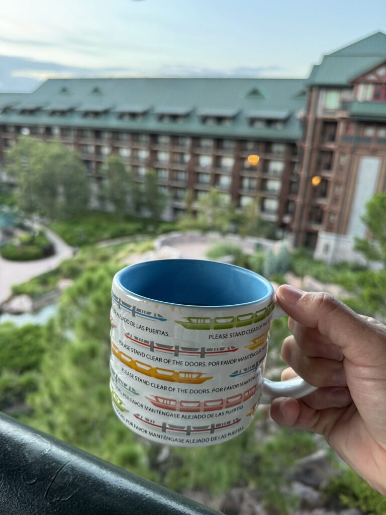 A mug with train designs being held out over the balcony of the Disney Wilderness Lodge Resort.