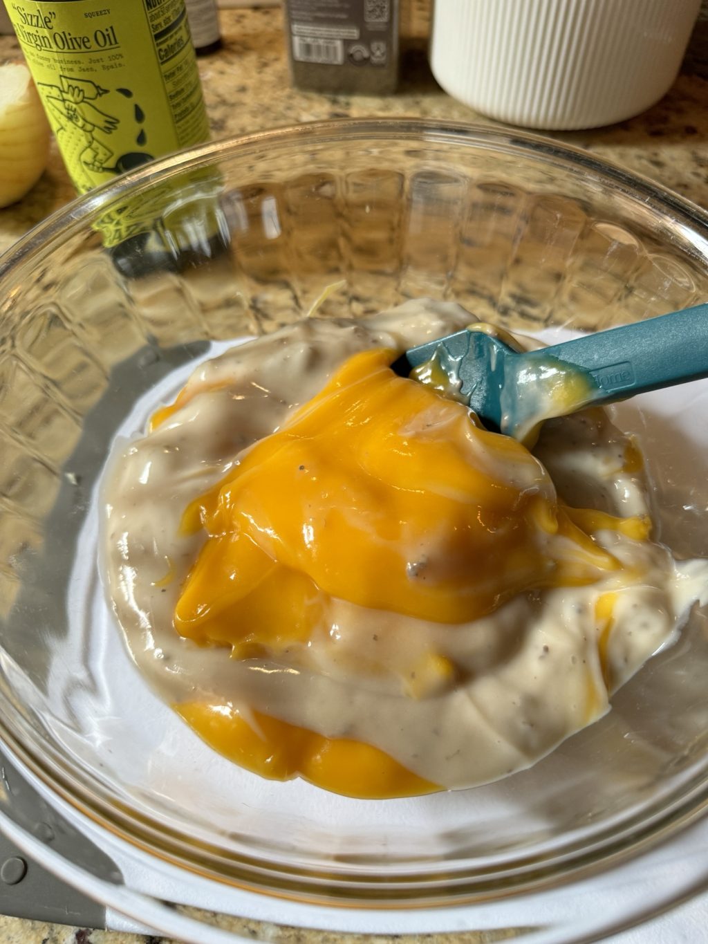 Campbell's Cheddar Soup and Campbell's Cream of Mushroom Soup together in a glass bowl with a blue spatula.