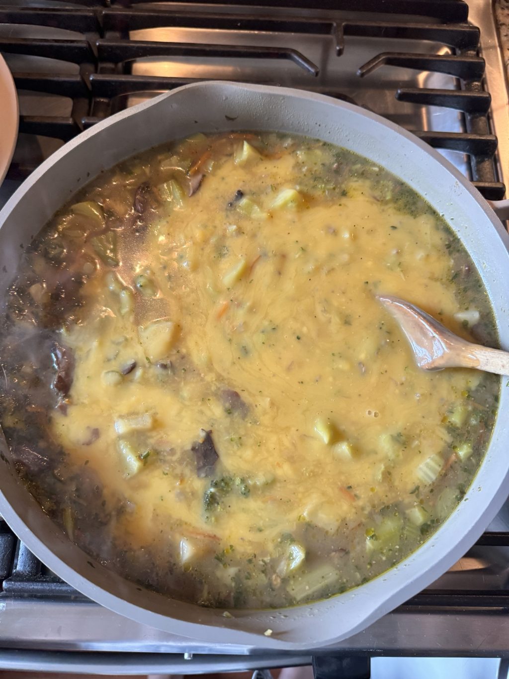 A pot of cheddar broccoli soup with a wooden ladle in it.