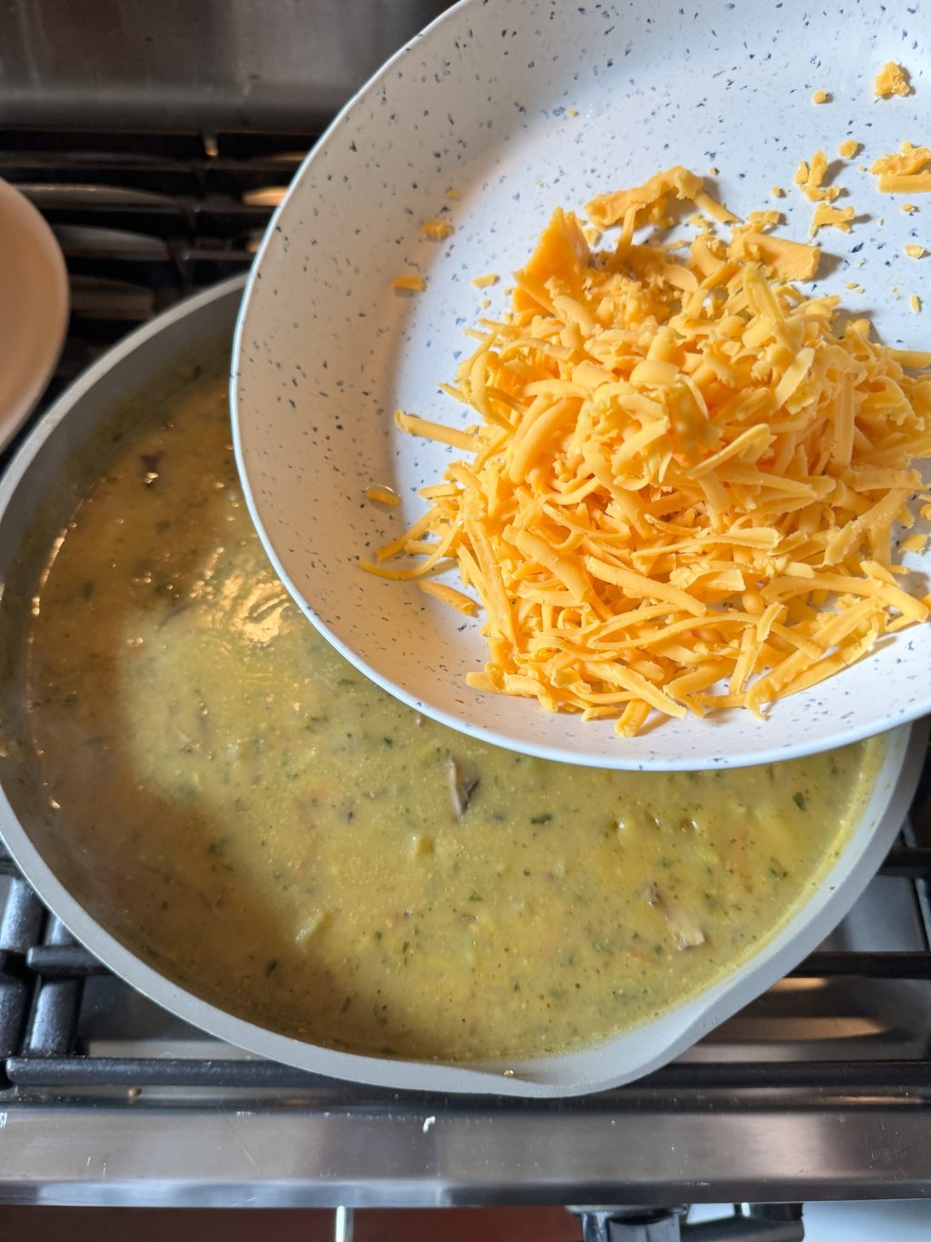 A bowl of shredded cheddar cheese about to be poured into a pot of soup.