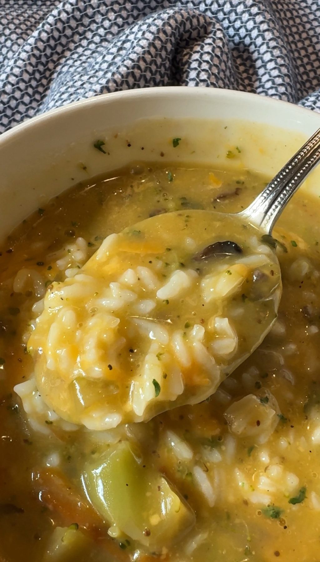 A close up of a spoon of broccoli cheddar soup with rice.