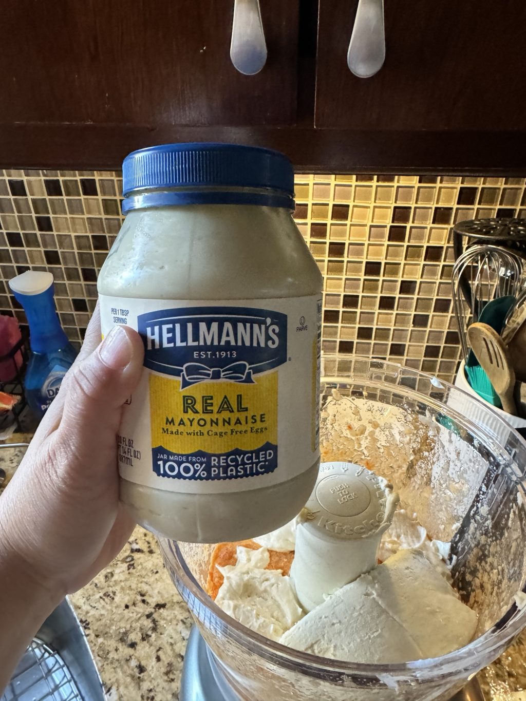 A jar of Hellman's mayonnaise being held over the food processor.