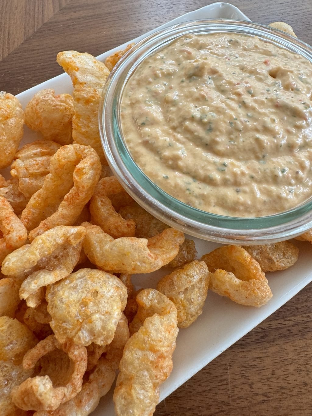 Pork rinds and pimento cheese dip on a rectangular plate.