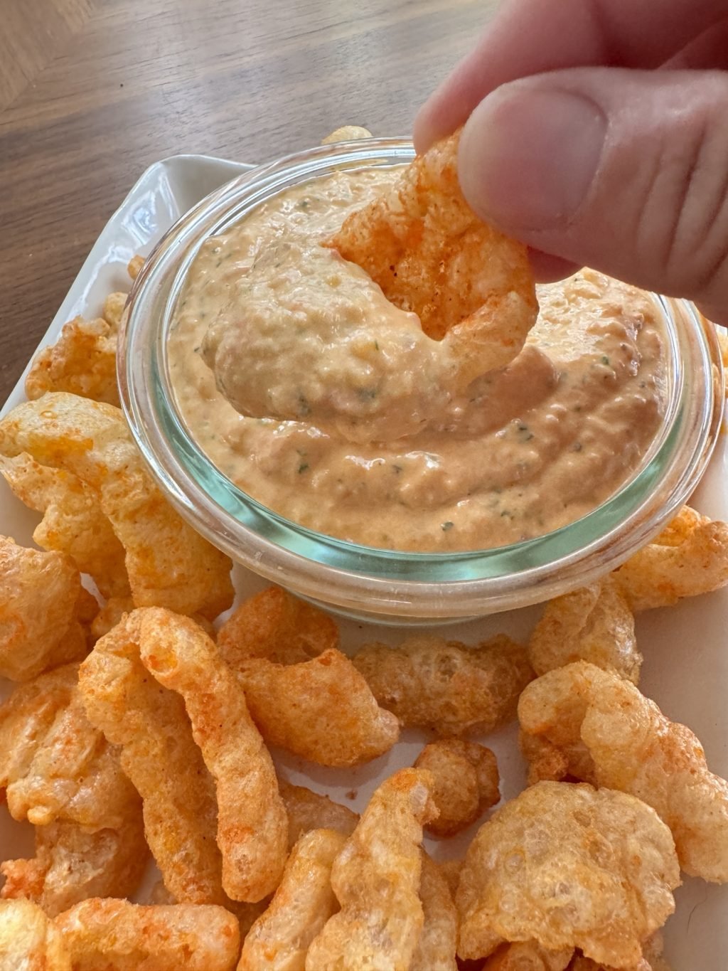 A spicy pork rind being dipped into pimento cheese dip.