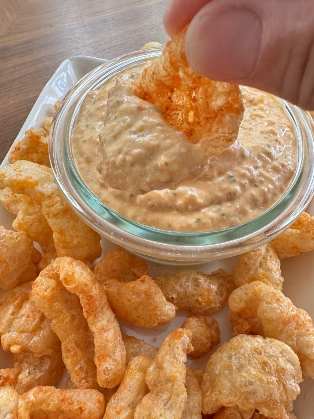 A spicy pork rind being dipped into pimento cheese dip.