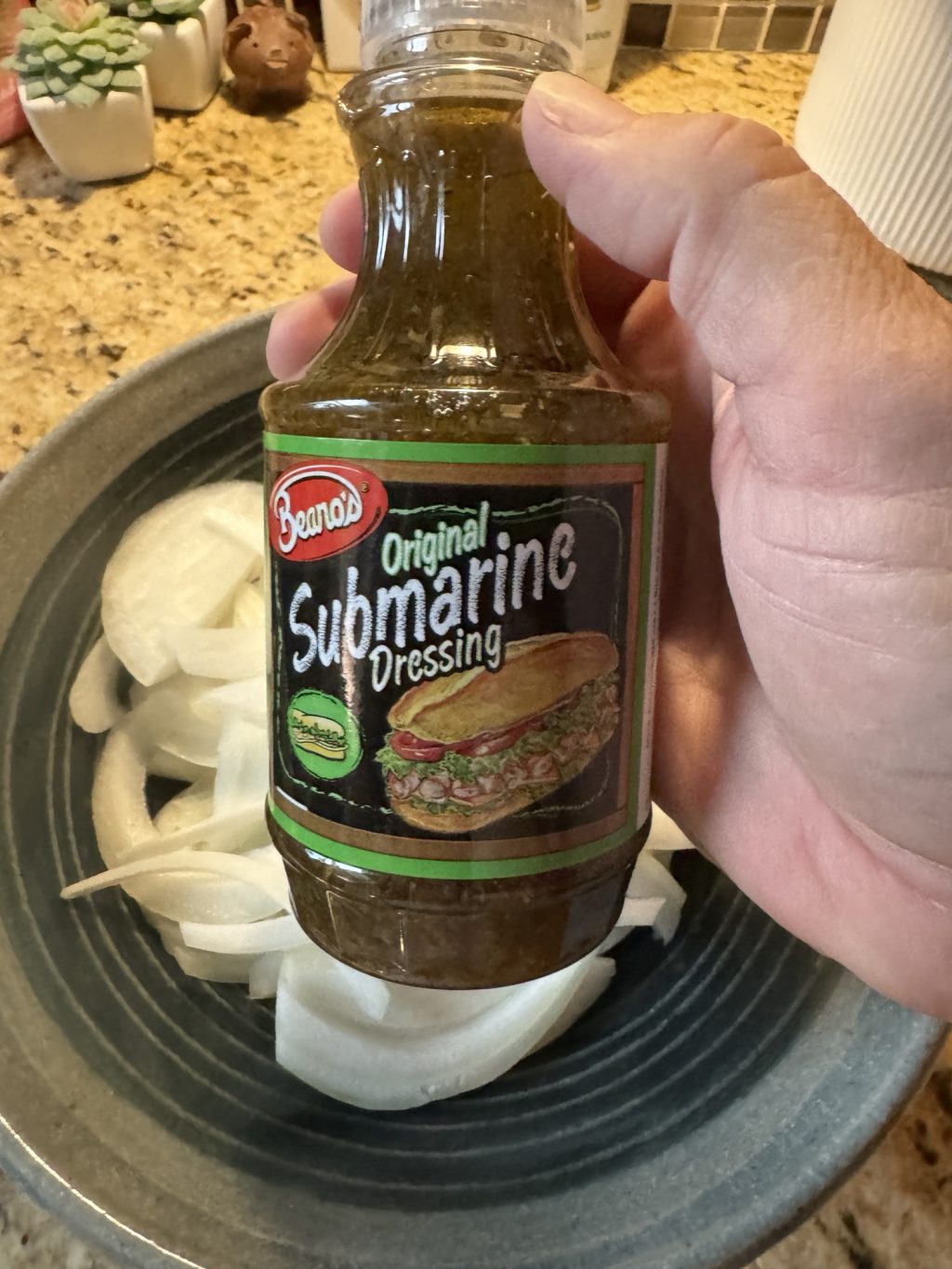 A bottle of Beano's Original Submarine Dressing held over a plate of onions.