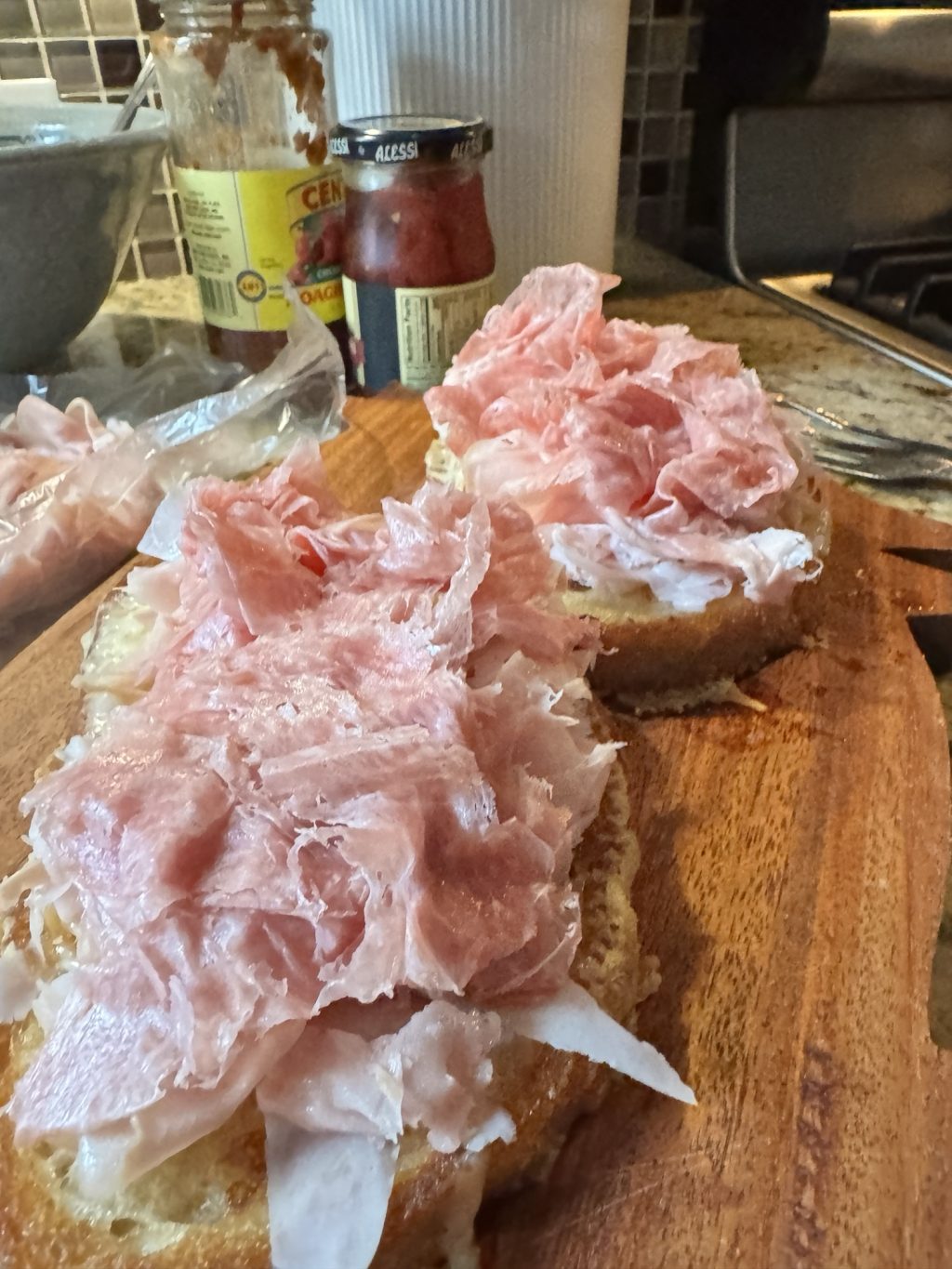 Deli meats spit be tween two breads on a wooden cutting board.